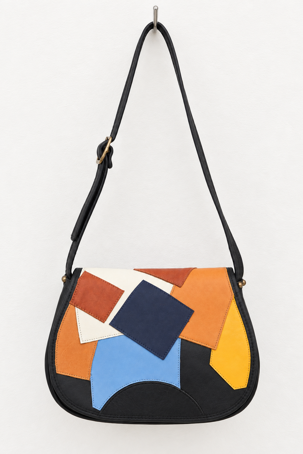 A black leather shoulder bag with an abstract geometric patchwork design on the front flap in orange, yellow, blue, white, and brown, shown hanging against a plain white background.