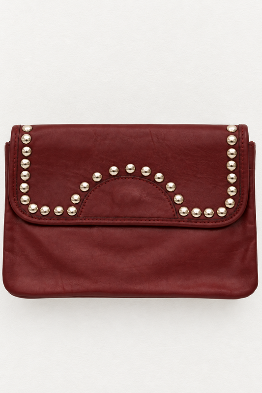A burgundy leather clutch bag with silver-tone metal studs arranged in a semicircle on the front flap, set against a plain light gray background.